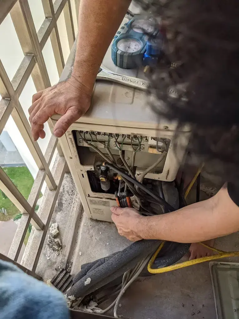 Technician inspecting an outdoor condenser unit and connection points at a service ledge.