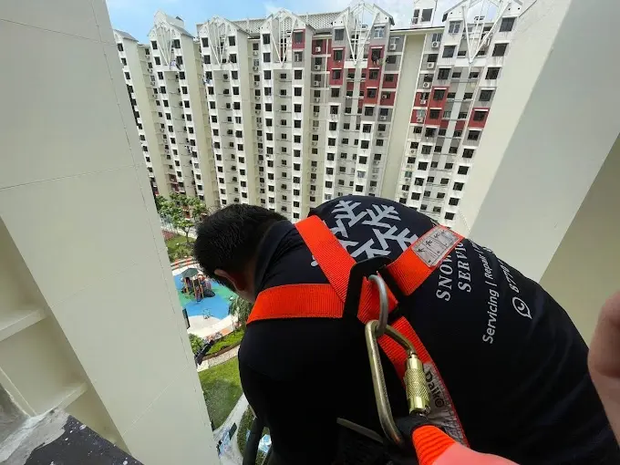 Technician using safety harness for high-rise external access to inspect an outdoor unit.