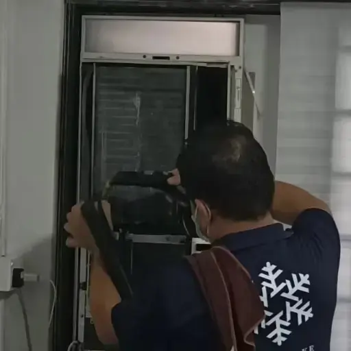 Technician performing a chemical wash on a window-type aircon unit.